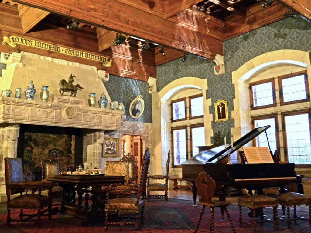 Inside the Chateau Menthon - a grand piano and richly coloured walls, a huge stone fireplace and dark wood furniture 