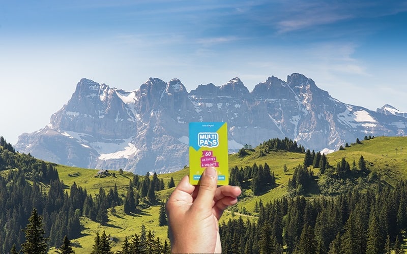A hand holds a multipass in front of some mountains