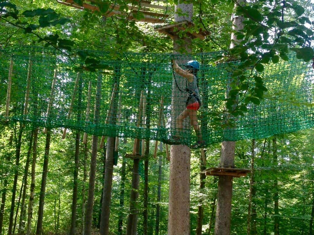 A child wearing a harness and helmet tackles a tree-top adventure course