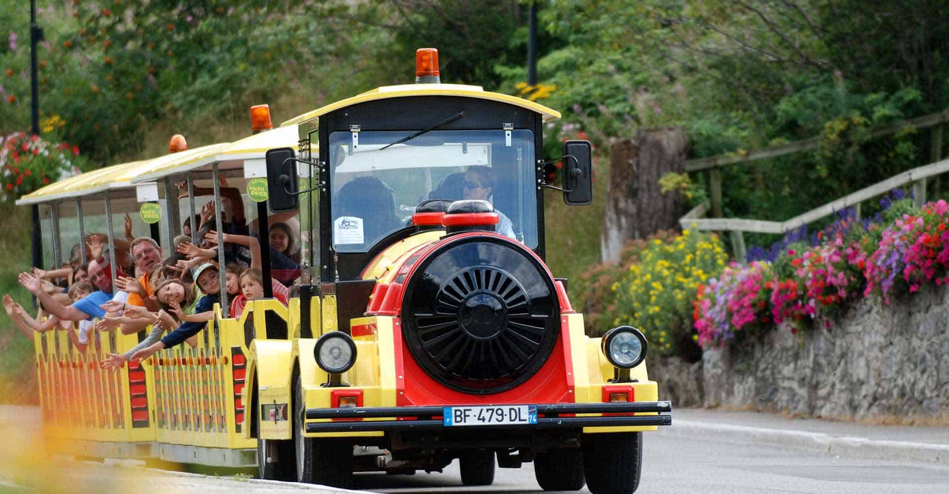 Un petit train jaune et rouge remplie de personnes en été.