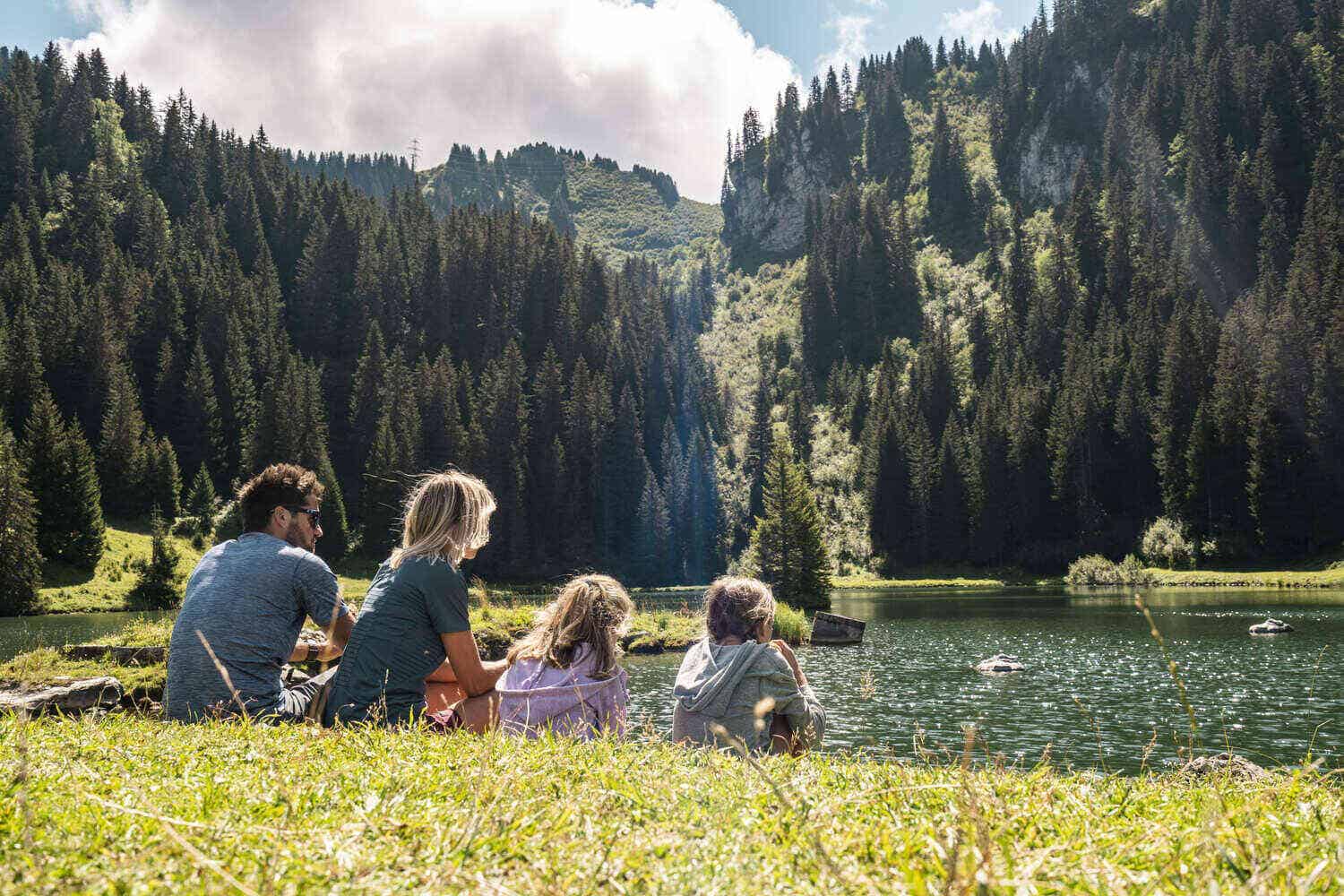 A family sitting on the grass at the side of a mountain lake