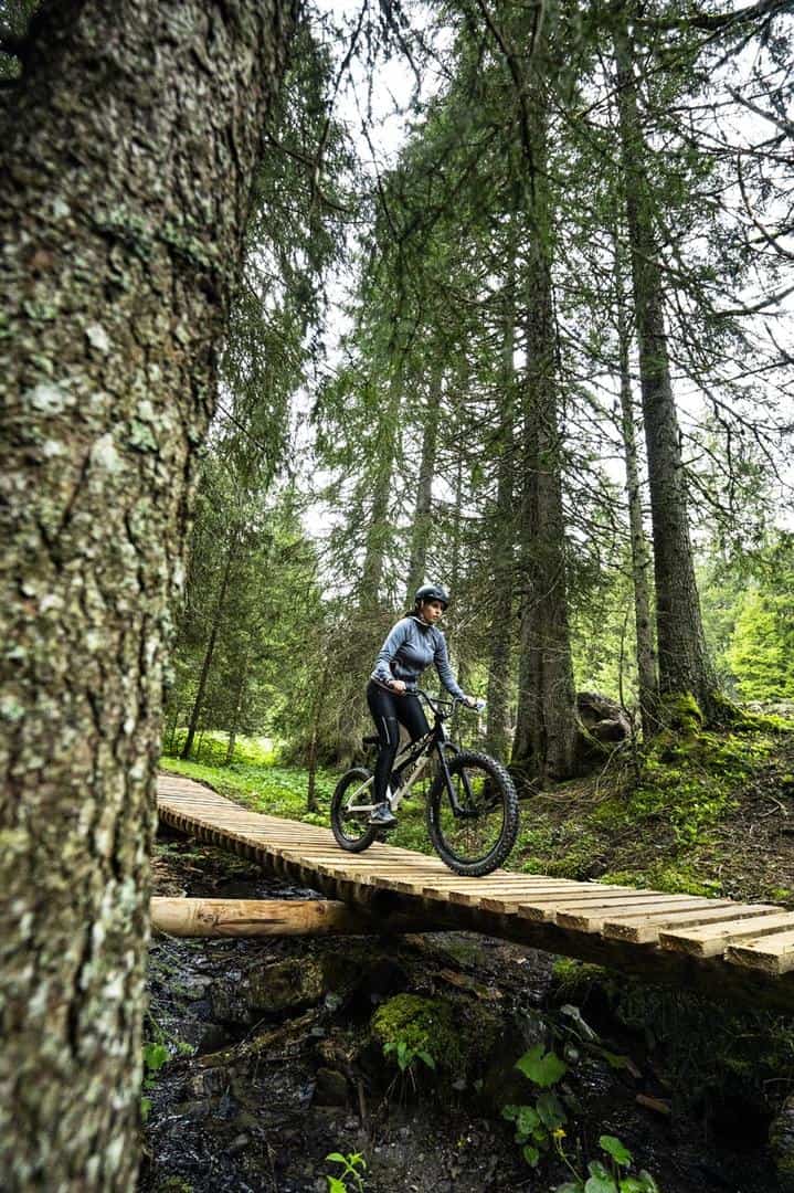 Une jeune femme à VTT dans la forêt, passant sur un pont en bois.