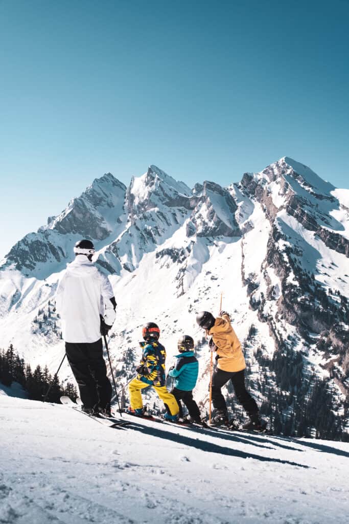A family stand on a ski slope pointing at a mountain