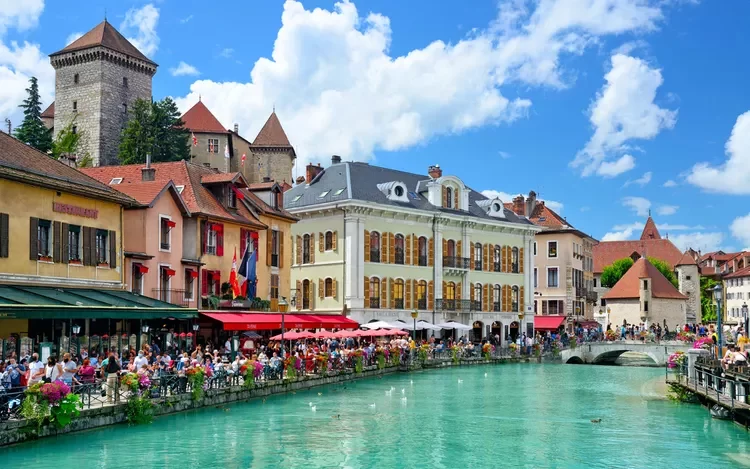 Families enjoy a meal at a canalside restaurant in the old town of Annecy