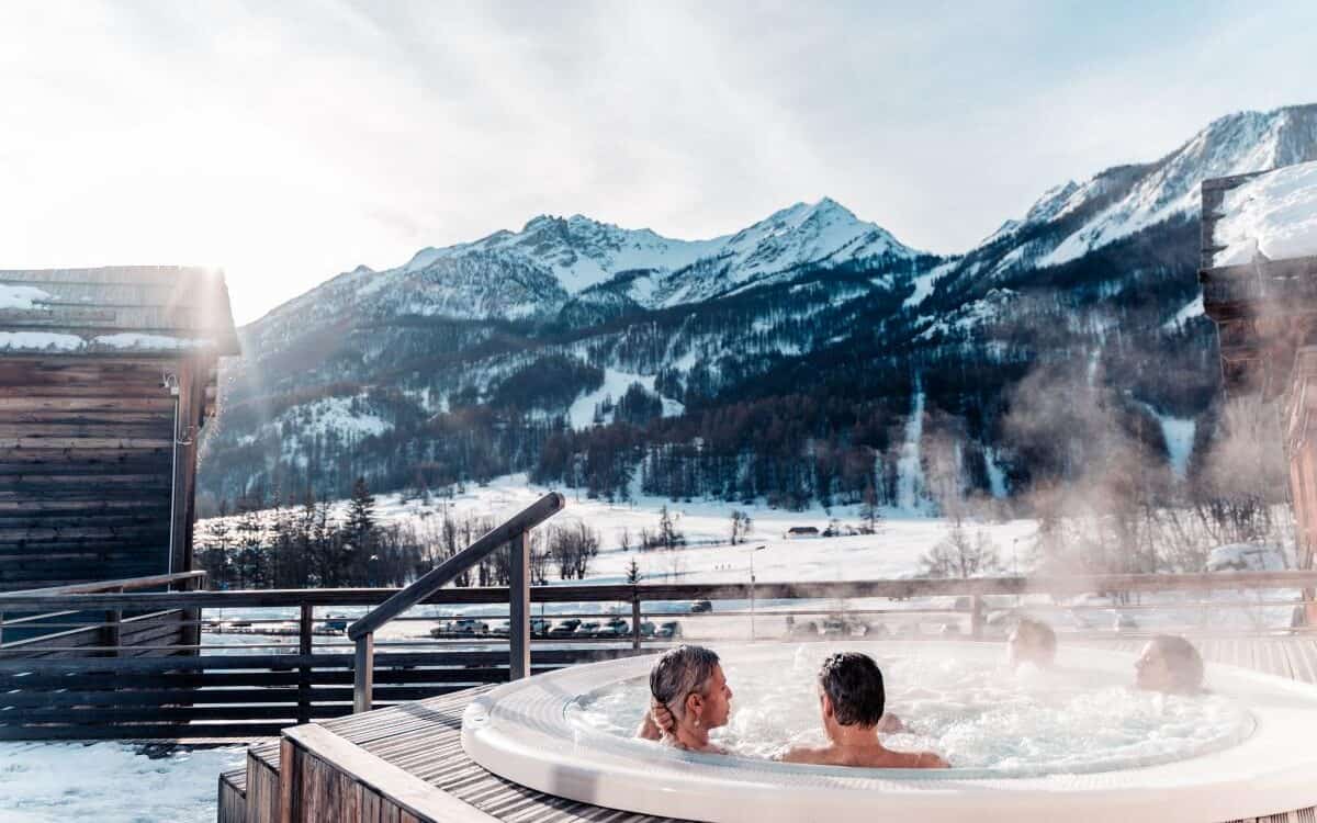 Four people relax in a hot tub with views of the mountains