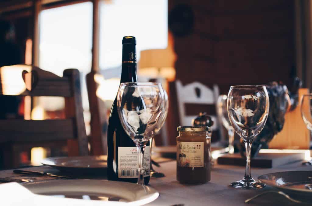 A bottle of wine with glasses and French honey sits on a table at a mountain restaurant