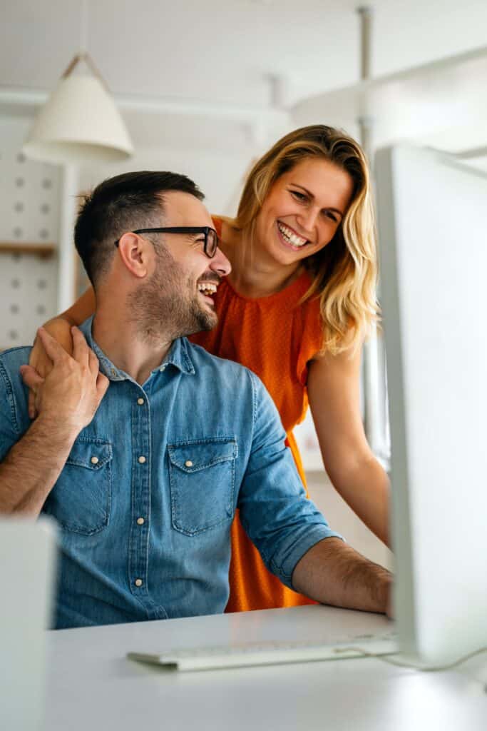 Un couple souriant devant un ordinateur. 
