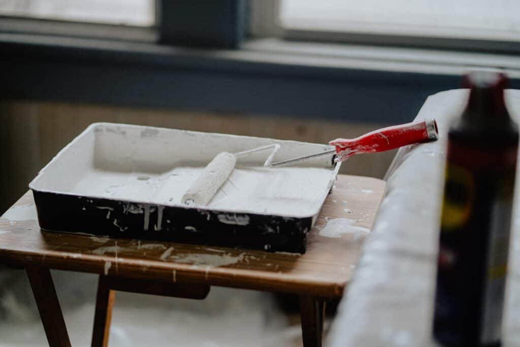 Un rouleau dans un bac de peinture blanche : de petites rénovations sont souvent à inclure dans le coût de la location d'un appartement au ski.