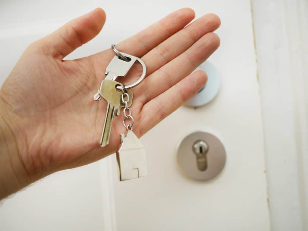 Une main, paume ouverte, tient un trousseau de clés devant la porte blanche d'un appartement au ski.