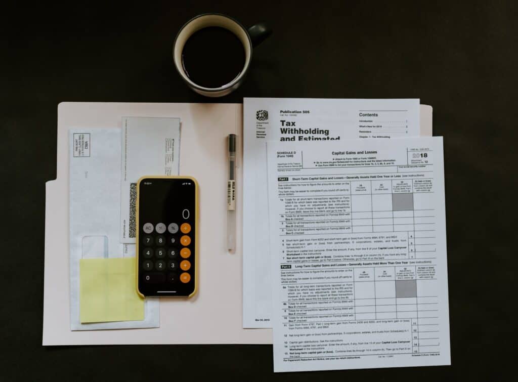 A folder, calculator and tax documents on a desk with a cup of coffee