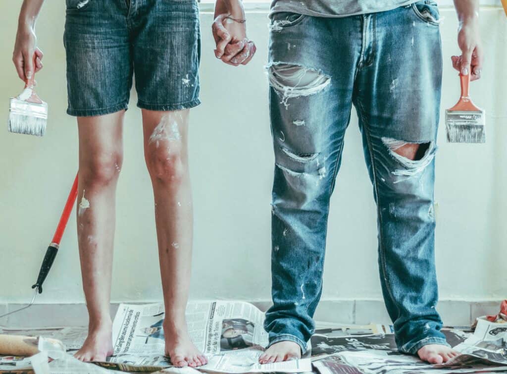 Paint-spattered legs of two people who have been painting a room