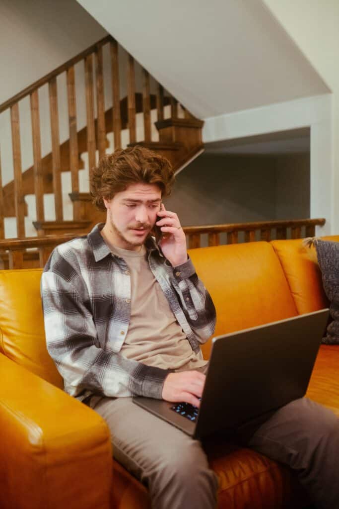 Un homme assis sur un canapé avec un téléphone et un ordinateur portable.