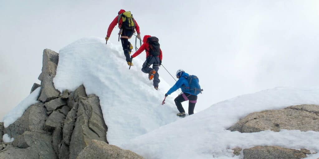 Three climbers roped together head up a snow-covered rock face