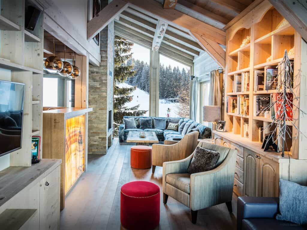 A cosy living room with a sloping ceiling, book cases, a TV area and a view of the slopes
