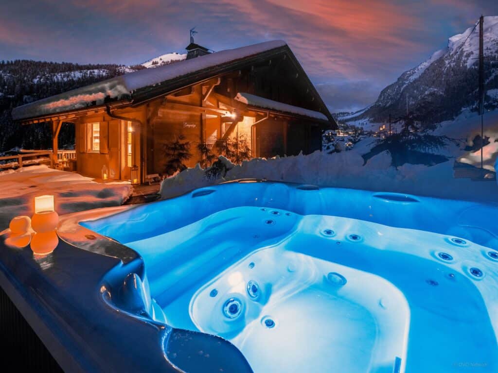 An illuminated hot tub outside a chalet at night