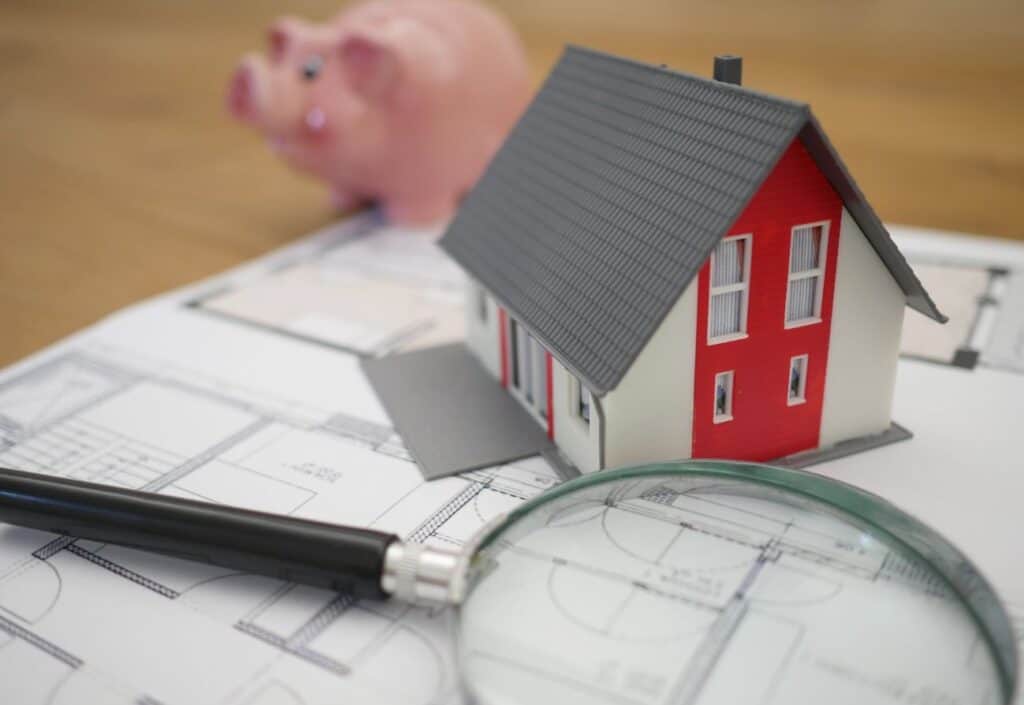 A magnifying glass, a model house, property plans and a piggy bank