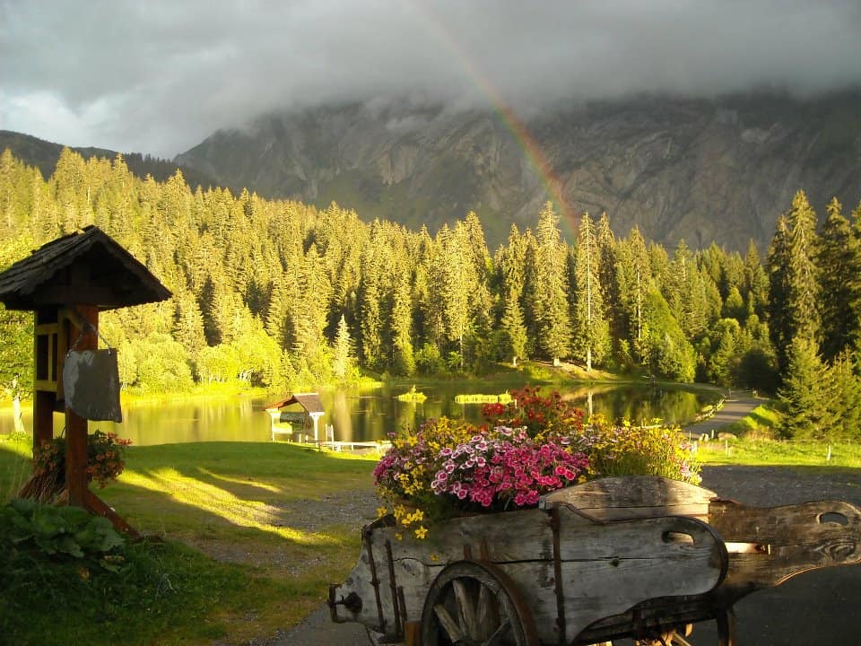 The Lac des Mines d'Or in Morzine - clouds hang over the mountains and a rainbow disappears into the trees