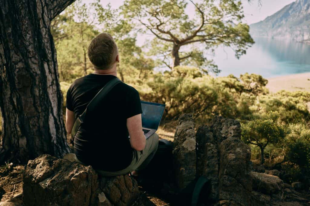 A man sits on a laptop in nature