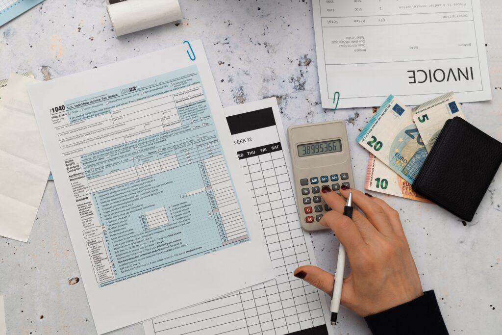 A hand types on a calculator with invoices and notes around it