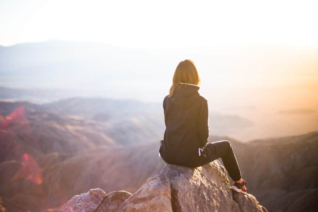 A woman sits on a rock at the top of a mountain