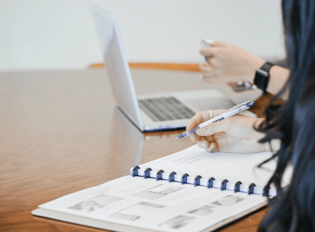 Two people, one with a notebook and one with a laptop, work together at a table