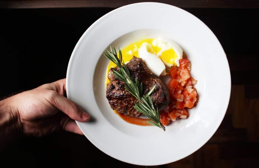 A hand holds a plate of meat, eggs and veg