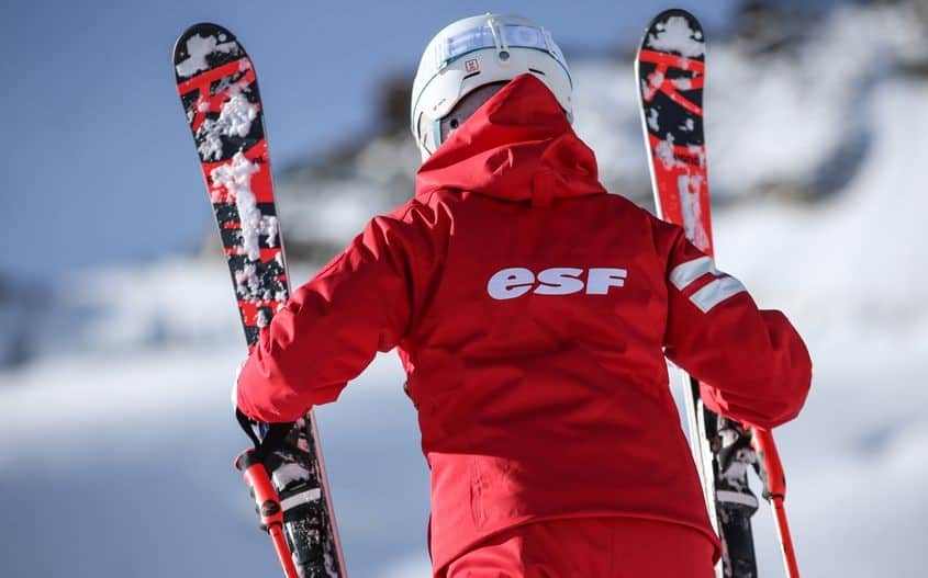 An ESF ski instructor wearing the famous red ski suit and carrying his skis