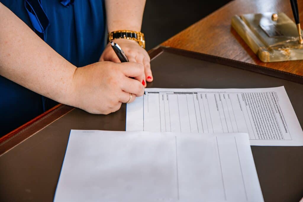 A woman signs papers on a wooden table