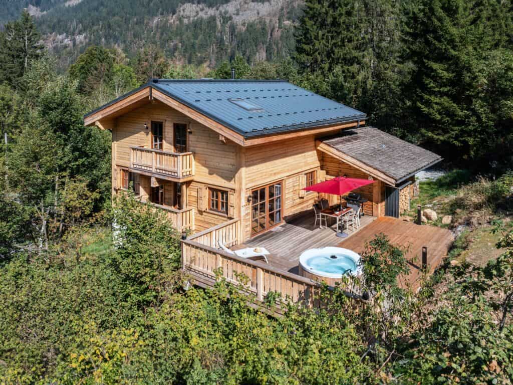Vue d'oiseau d'un chalet Airbnb isolé à la montagne, avec jacuzzi sur une terrasse en bois.