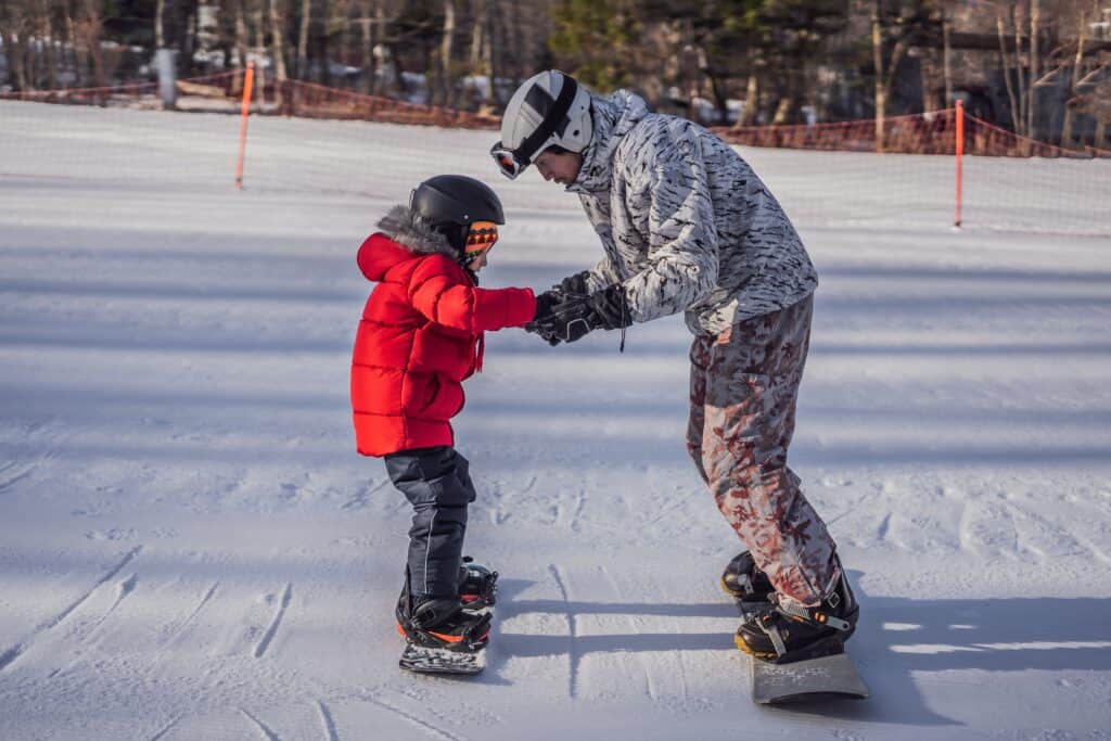 A kid learns to snowboard with an instructor