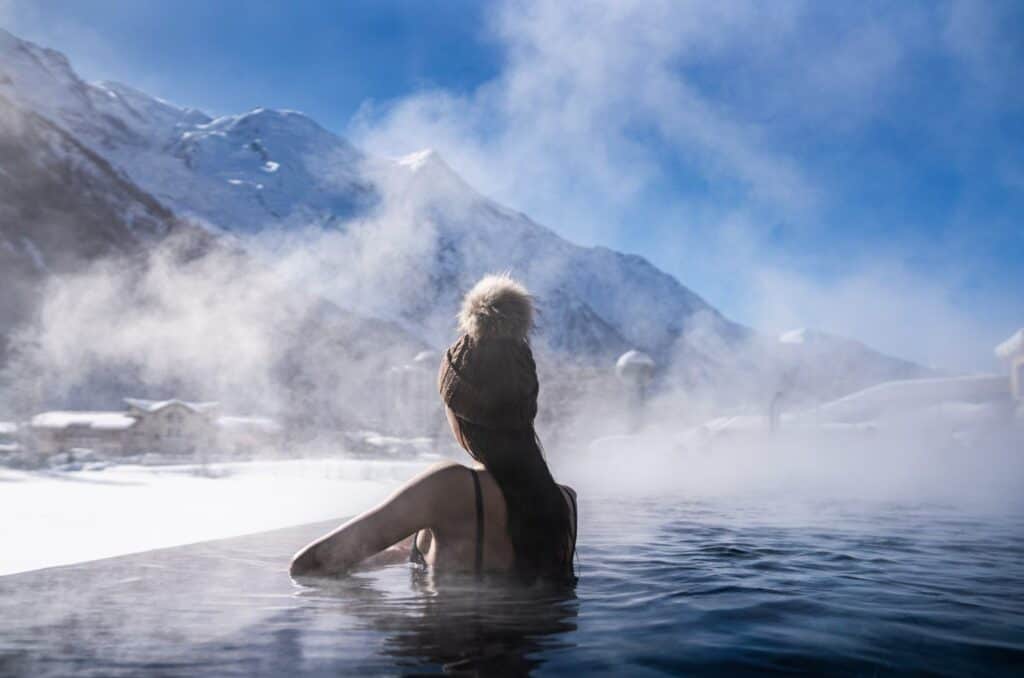 A woman relaxes in a thermal pool, and admires the mountain view