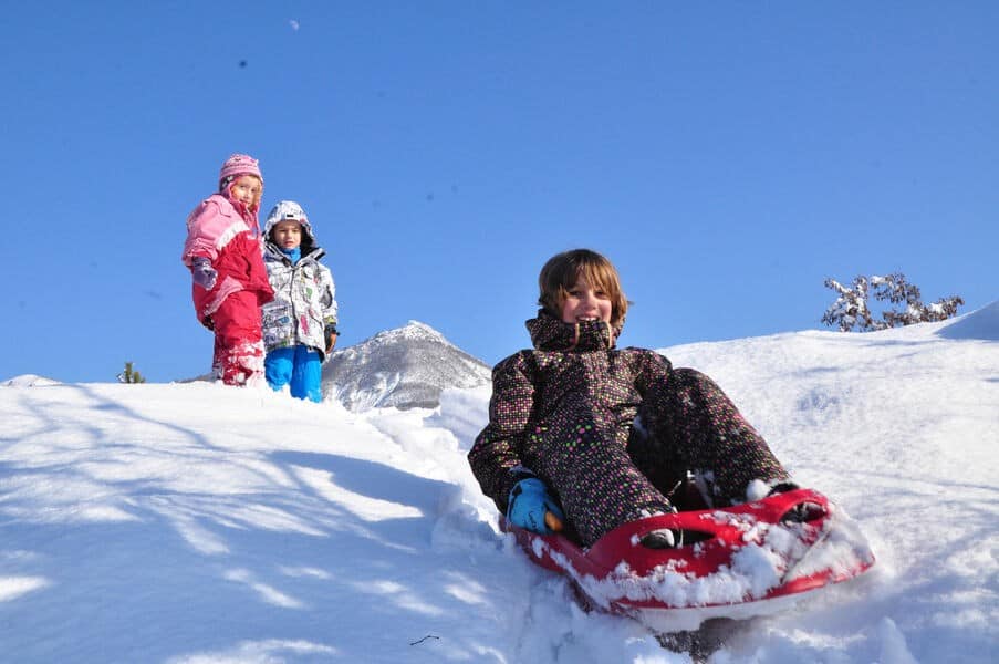 Two children watch as another sledges down a snowy hill