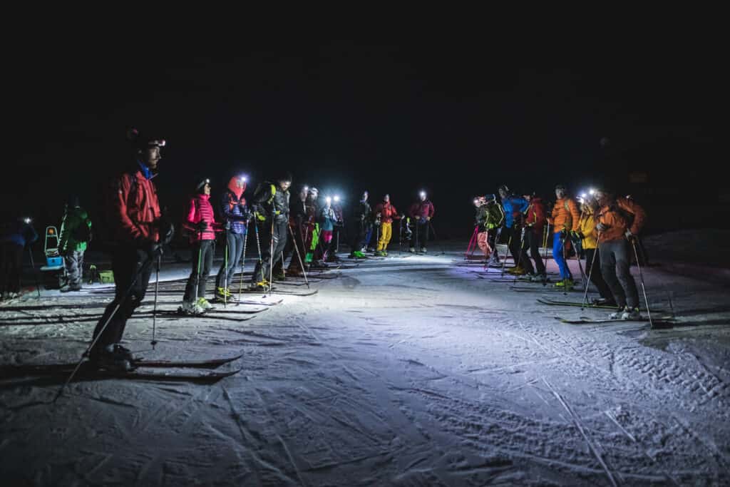 A group of people gathered on a ski slope at night wearing head torches