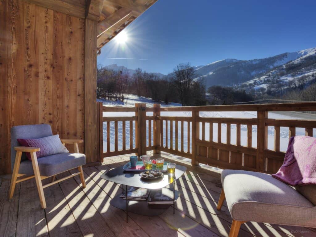 A table with drinks and snacks, and chairs on a sunny terrace of a chalet with mountain views