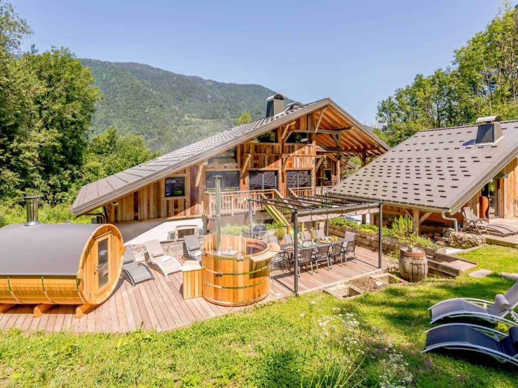 A large terrace at the back of a chalet with a hot tub, Nordic bath, dining table and chairs and sunbeds