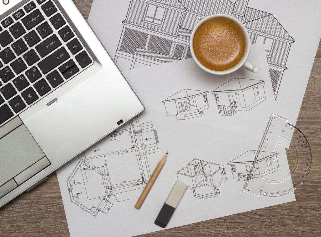 A desk covered with architect's drawings, a laptop and a cup of coffee