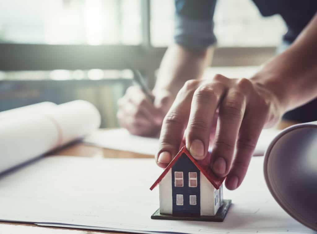 The hand of a person putting a model house down on a piece of paper