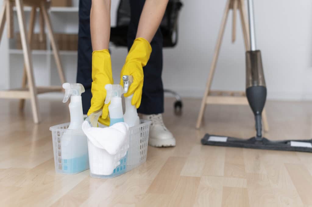 A person wearing rubber gloves with a vacuum cleaner and a selection of cleaning products