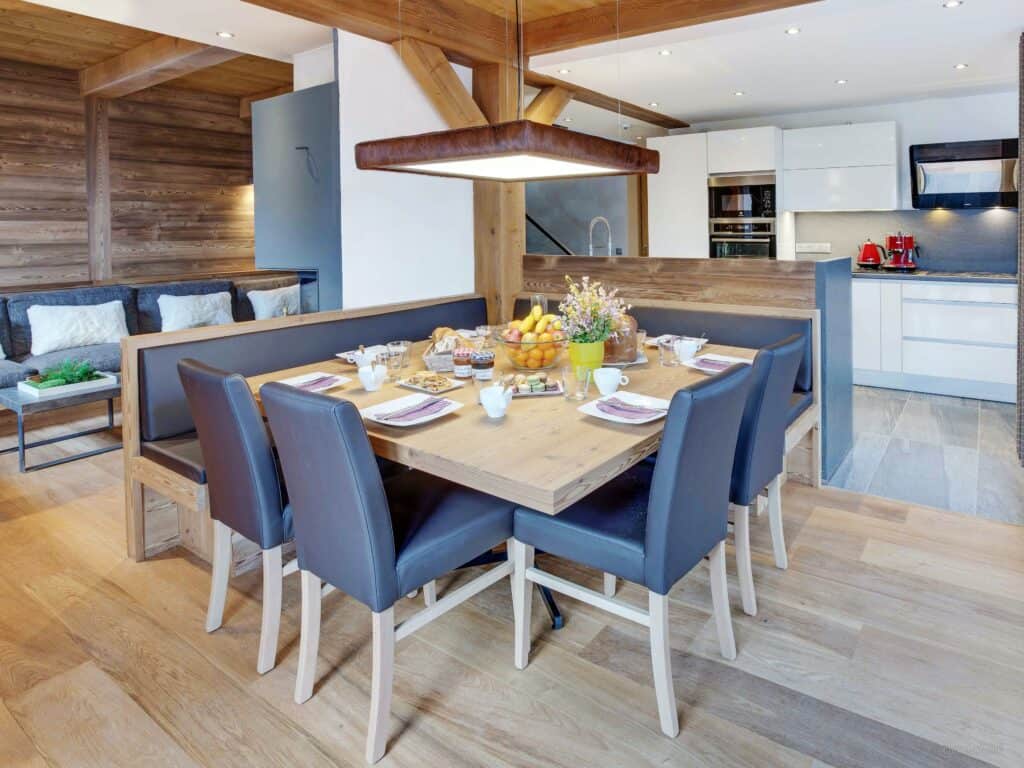 A dining area with chairs and bench seating and a kitchen behind it