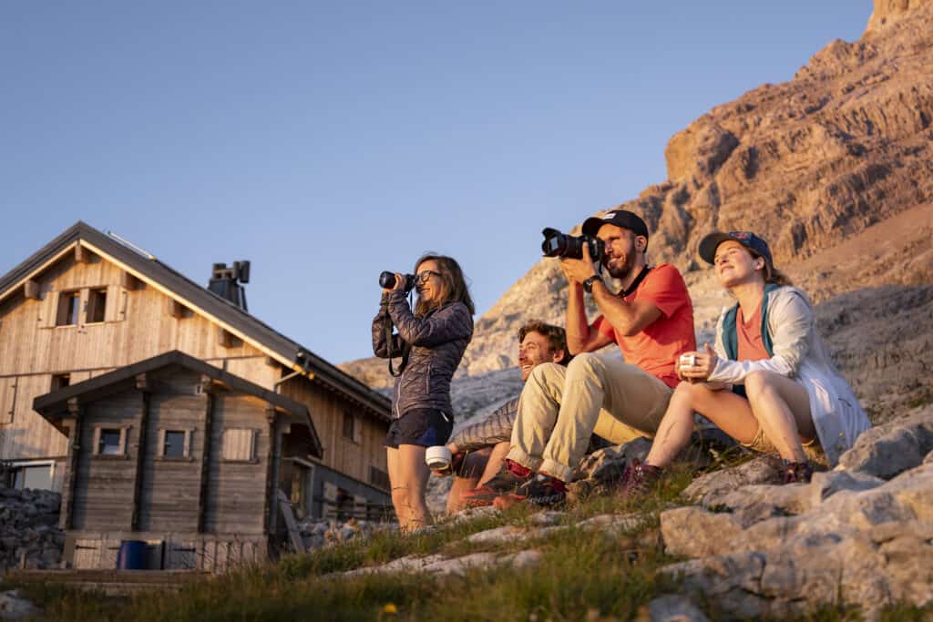 A group of friends take photos as the sun sets on the mountains