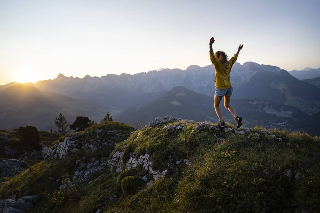 A woman stands on a  mountain with her hands in the air