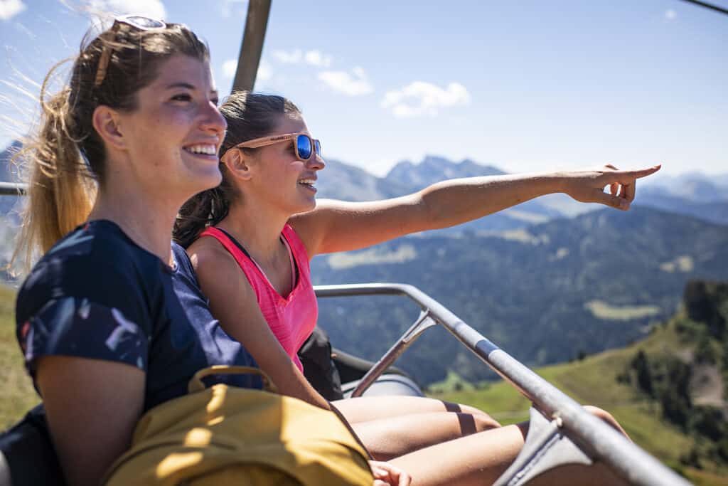 Two women take a chairlift and point to views in the distance