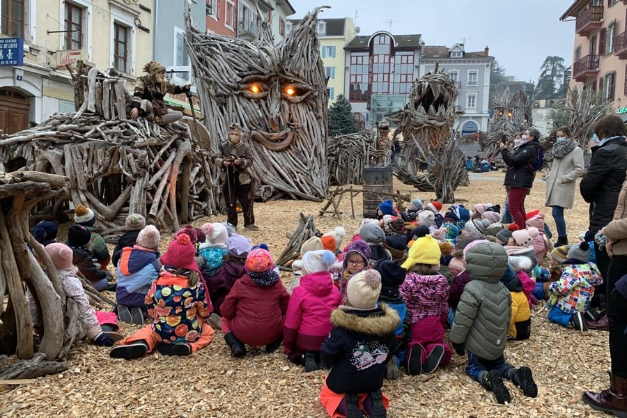 Group of children sitting around wooden sculptures for a show.